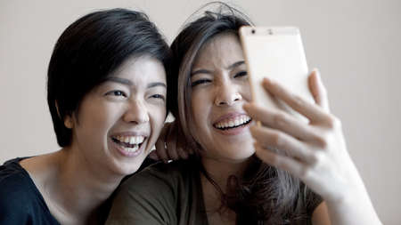 Two mixed race Asian girls taking selfie with smart phoneの写真素材