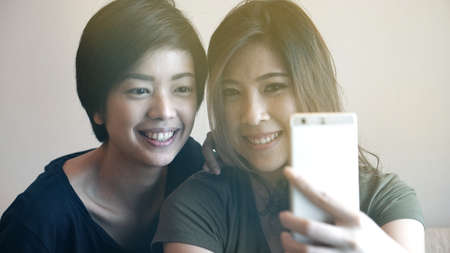 Two Asian woman taking photo, selfie using cell phone の写真素材