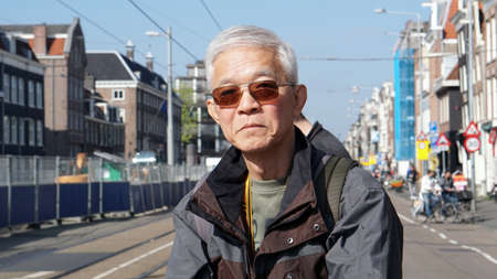 Asian senior man take a solo trip to Amsterdam, Netherlands waiting for tram transportationの写真素材