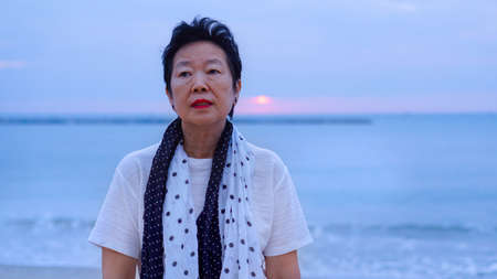 Asian senior standing alone and thinking at mornign beach sunriseの写真素材