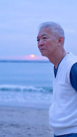 Asian senior standing alone and thinking at mornign beach sunrise