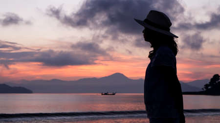 Asian woman silhouette at sunrise ocean pink and orange skyの写真素材