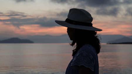 Asian woman silhouette at sunrise ocean pink and orange skyの写真素材