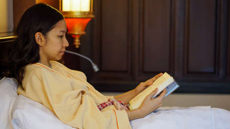 Asian woman reading book on bed with cozy interior lightの写真素材