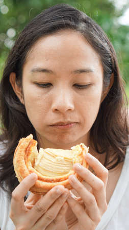 Asian woman holding and eating fresh baked bread bakery in green background parkの写真素材