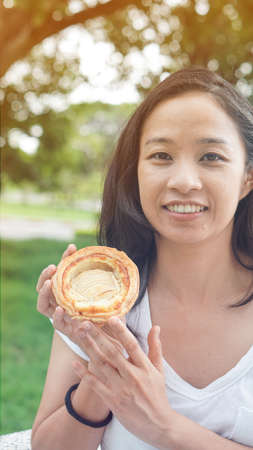 Asian woman holding and eating fresh baked bread bakery in green background parkの写真素材