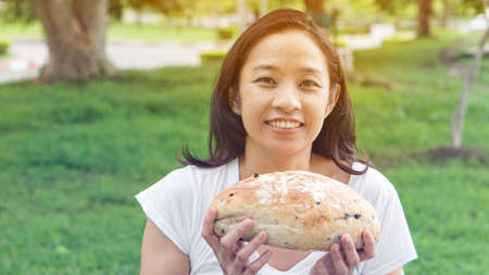 Asian woman holding and eating fresh baked bread bakery in green background parkの写真素材