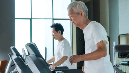 Old healthy Asian senior couple exercise together in gym running treadmillの写真素材