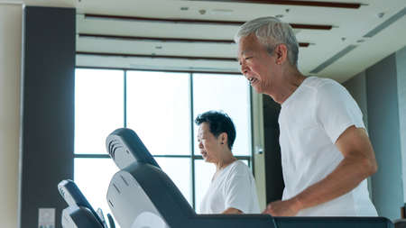 Old healthy Asian senior couple exercise together in gym running treadmillの写真素材