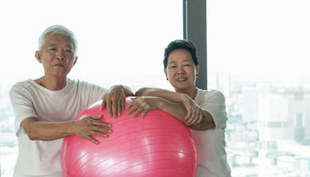 Happy old senior Asian couple have fun with gym yoga ball classの写真素材