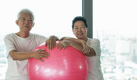 Happy old senior Asian couple have fun with gym yoga ball classの写真素材