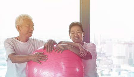 Happy old senior Asian couple have fun with gym yoga ball classの写真素材