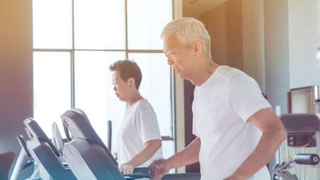 Old healthy Asian senior couple exercise together in gym running treadmill