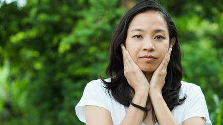 Asian woman long hair facial epression green nature backgroundの写真素材