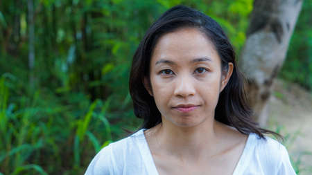 Asian woman long hair facial epression green nature backgroundの写真素材