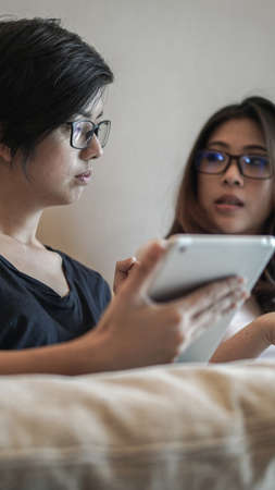 Two Asian friends watching thing on tablet and computer sharing idea at homeの写真素材