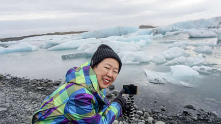 Asian old woman happy taking photo with smartphone glacier lagoon, Icelandの写真素材