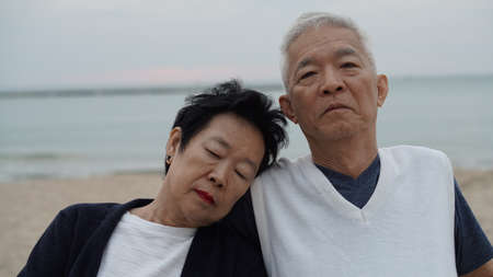 Asian senior elderly couple resting together next to ocean backgroundの写真素材