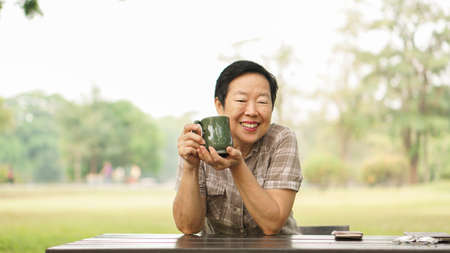 Asian senior woman smiling in park wiht coffee cup