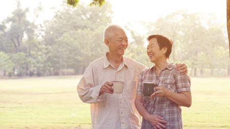 Asian senior couple relax drinking coffee in summer park, green background