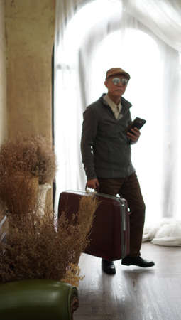 Asian senior business man with vintage luggage and smart phone working while on vacationの写真素材