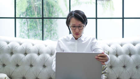 Freelance Asian woman working notebook computer at home sofaの写真素材