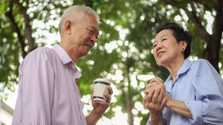 Happy Asian elderly couple morning walk in green city drinking coffee and talkingの写真素材