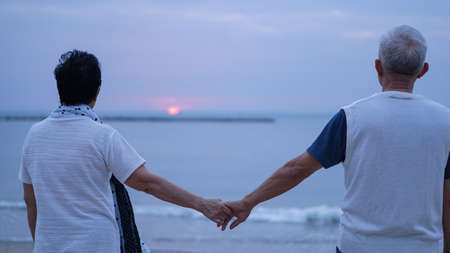 Asian elderly couple hold hand at beach ocean sunriseの写真素材