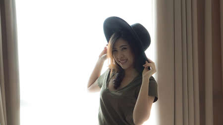 Asian mixed race woman long hair wear hat at home curtain light windowの写真素材