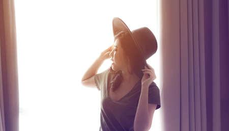 Asian mixed race woman long hair wear hat at home curtain light windowの写真素材