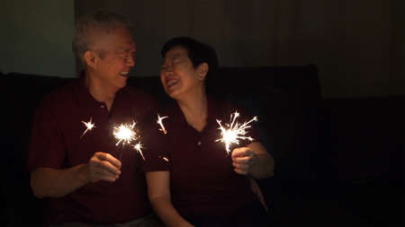 Asian senior couple celebrating together at home sparkles fireworkの写真素材