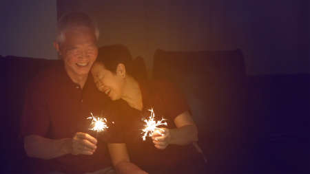 Asian senior couple celebrating together at home sparkles fireworkの写真素材