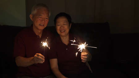 Asian senior couple celebrating together at home sparkles fireworkの写真素材