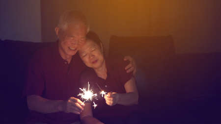 Asian senior couple celebrating together at home sparkles fireworkの写真素材