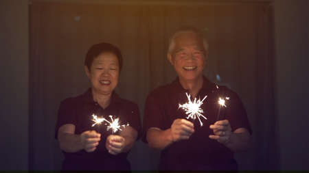 Asian senior couple playing firework, sparklers, fire cracker at night. Concept celebrating lifeの写真素材
