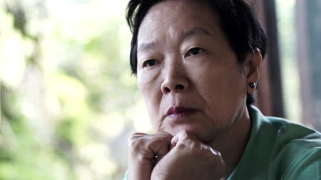 Asian senior woman with hand on face thinking, worry and sadの写真素材