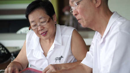 Asian senior couple reading books and magazines together in small library. Learning and study...