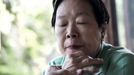 Asian senior woman with hand on face thinking, worry and sadの写真素材