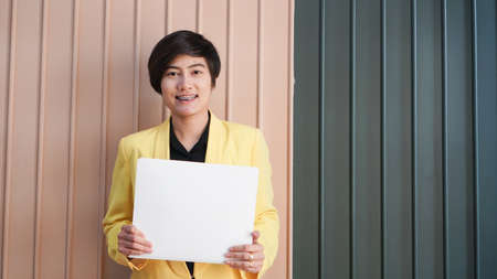 Working Asian smart woman in yellow suit holding white copy space card in luxury interior backgroundの写真素材