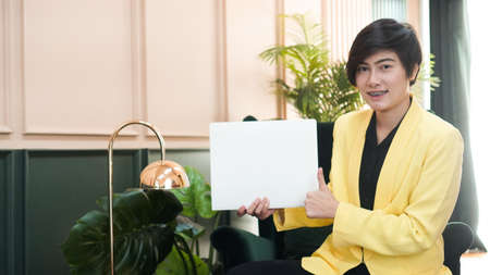 Working Asian smart woman in yellow suit holding white copy space card in luxury interior backgroundの写真素材