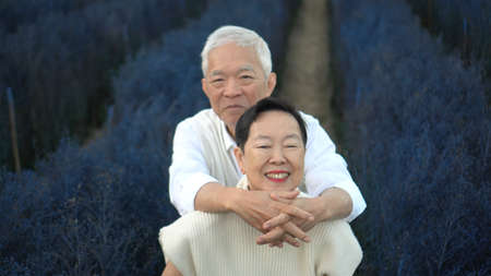 Asian retired senior couple hugging celebrating love in magical blue flower fieldの写真素材