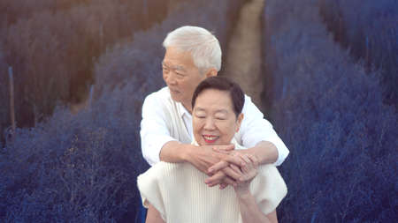 Asian retired senior couple hugging celebrating love in magical blue flower fieldの写真素材