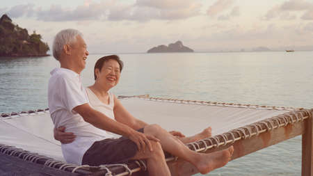 Asian senior couple sitting at sunrise sea early morning relaxed happy natural retirementの写真素材