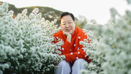 Elder beautiful Asian woman wearing seasonal holiday red sweater with white dots to celebeate chirstmas outdoor flower fieldの写真素材