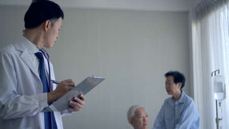 Asian young doctor writing down senior symptom disease note planning medical planの写真素材