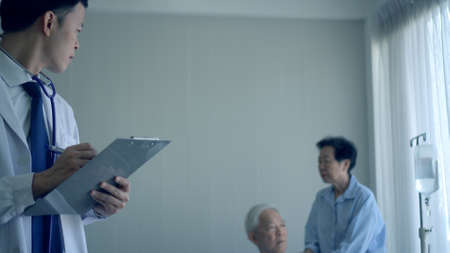 Asian young doctor writing down senior symptom disease note planning medical planの写真素材