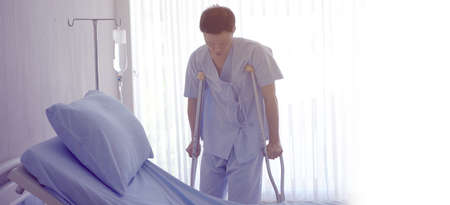 Adult Asian man physical injure walking with crutches while recover in hospital room aloneの写真素材