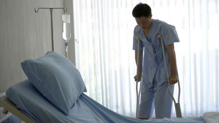 Adult Asian man physical injure walking with crutches while recover in hospital room aloneの写真素材