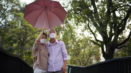 Asian senior elder couple walking in raining park share umbrella romantic love lifestyleの写真素材