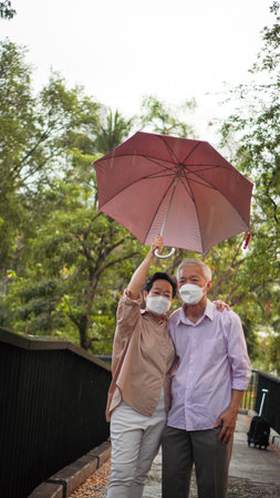 Asian senior elder couple walking in raining park share umbrella romantic love lifestyleの写真素材